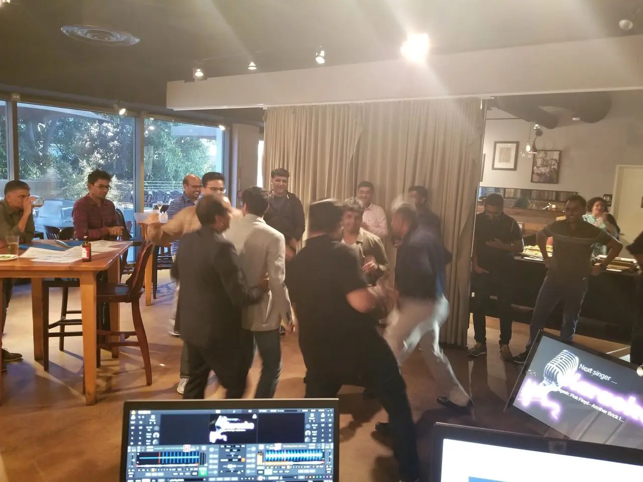 Mr Dj Services Karaoke A group of people, some standing and some sitting, gather inside a restaurant; several appear to be involved in an altercation while others watch. Computer monitors are visible in the foreground.