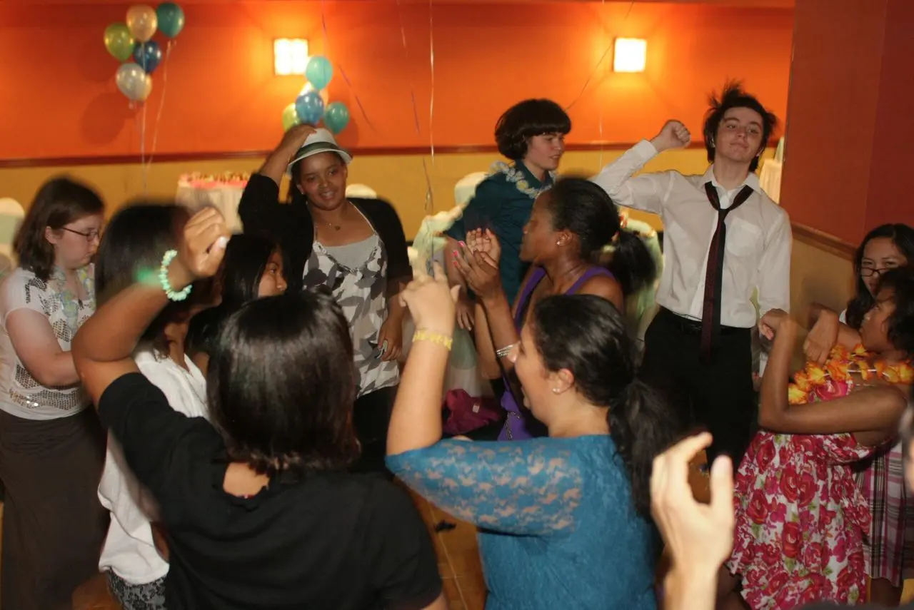 Sweet 16 Dance Party A group of people dance and celebrate together in a decorated room with balloons and orange walls.