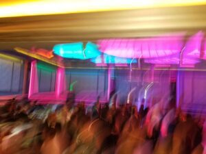 A blurred image shows a crowd under vibrant neon lights in shades of pink, blue, and yellow, creating an abstract effect.