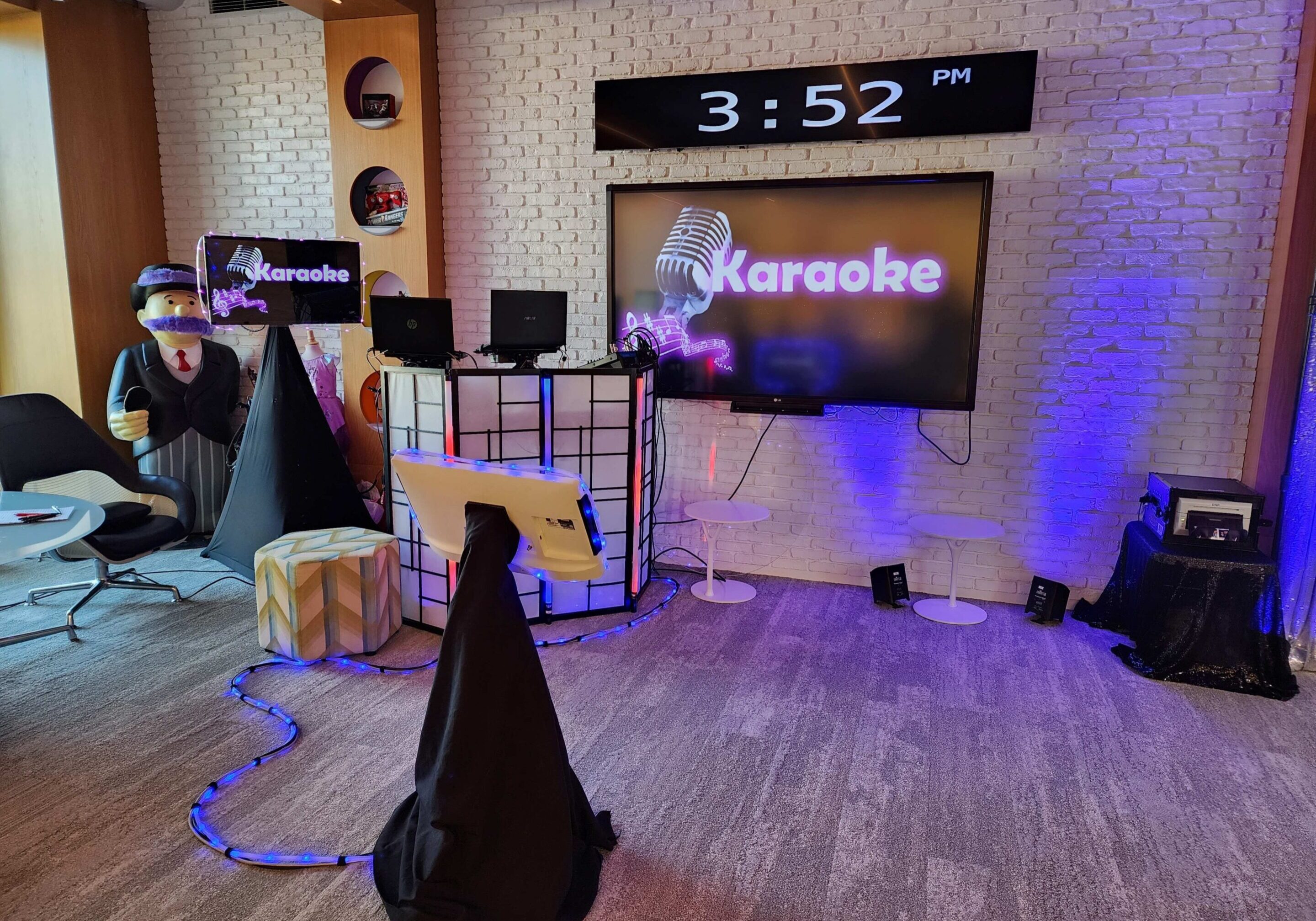 A modern karaoke dj setup in a room with a large screen displaying "Karaoke," two microphones, speakers at Hasbro Christmas Party.